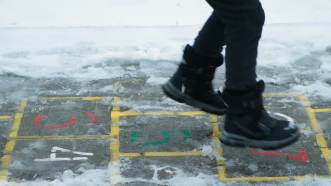 小孩子穿着靴子在外面下雪时蹦蹦跳跳。冬天的衣服，童鞋