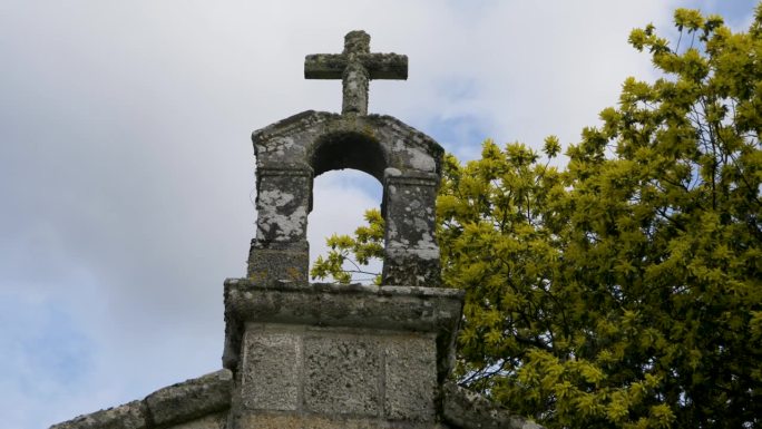 低角度仰望圣维托罗教堂雕刻的石头十字架、青苔和黄绿色的花朵