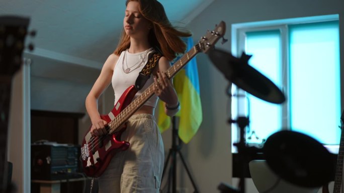 在一所音乐学校里，一名年轻女孩站在乌克兰国旗的背景下，精力充沛地弹着贝斯吉他。