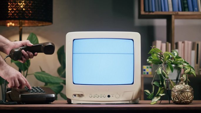 家庭背景是带有蓝色干扰屏的旧电视。餐桌上的老式电视特写，有植物，怀旧。男子用复古电话打电话。