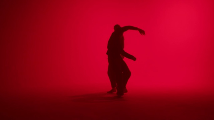 专业舞蹈编导在工作室的红色霓虹灯背景上跳舞。男女舞者表现出缓慢的动作，双人舞，二人转。青少年现代舞学