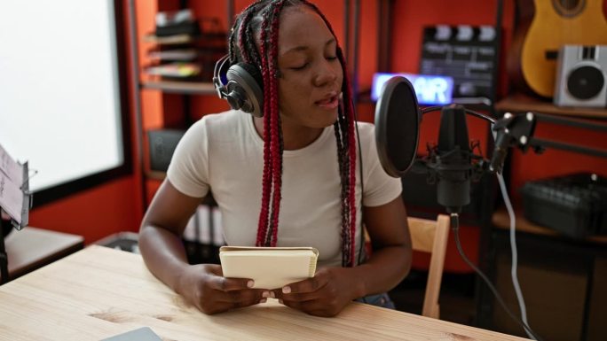 美丽的非裔美国女音乐家沉浸在歌曲中，在音乐工作室的声音幸福中阅读笔记本上的歌词