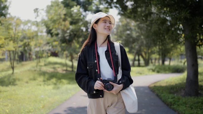 休闲风格的年轻亚洲女性在度假时站在自然公园用她的相机拍照。