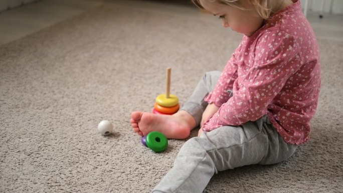 小女孩在家里、幼儿园或托儿所玩玩具。宝宝孩子玩玩具立方体和木头拼图，金字塔坐在地板上。快乐学前教育室