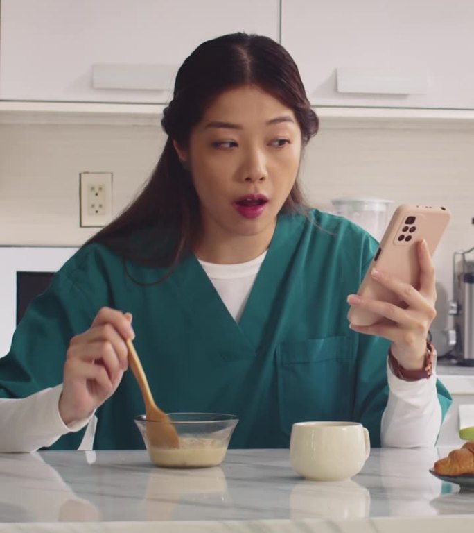 亚洲护士在厨房吃酸奶和使用电话