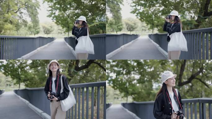 年轻的亚洲女游客站在公园的桥上拿着相机拍照