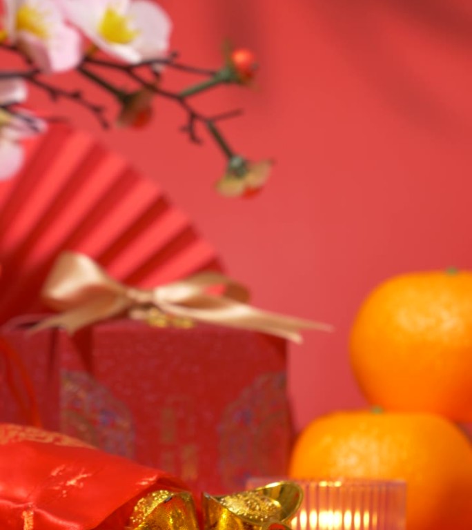 中国农历新年的背景。中国古代金条在丝绸袋，红色礼盒与金弓，纸扇，橘子，梅花枝，蜡烛和树叶的影子摇摆。