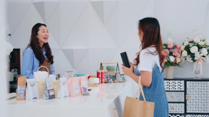 两名亚洲妇女在一家咖啡店的柜台前分享快乐的时刻，反映出友好的顾客服务和社区联系。
