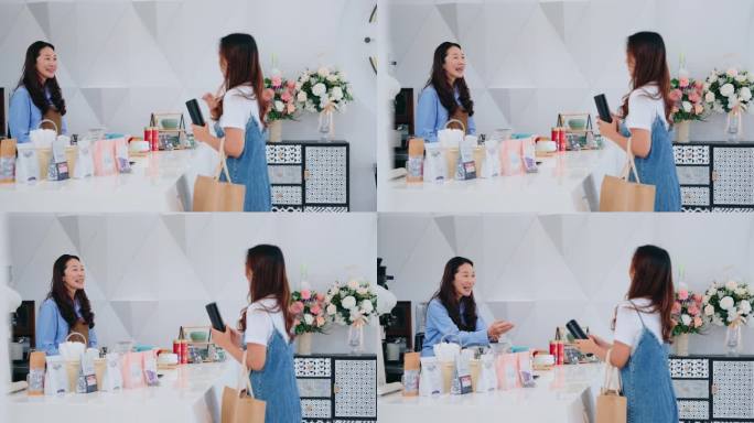 两名亚洲妇女在一家咖啡店的柜台前分享快乐的时刻，反映出友好的顾客服务和社区联系。