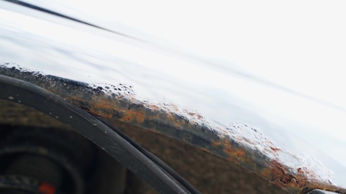 一辆黑色汽车的拱与通过腐蚀，底部视图。经过冬天，汽车的挡泥板被腐蚀了，橡胶密封件下面有湿气。试剂对车