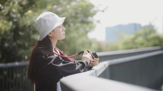 年轻的亚洲女子拿着相机站在自然公园的桥上