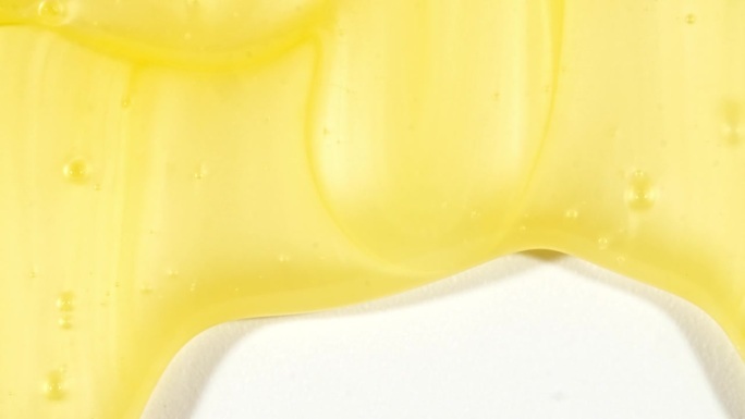 黄色透明化妆品凝胶液体与分子气泡流动在白色的表面。微距镜头。液体乳霜凝胶透明化妆品样品纹理与泡沫。
