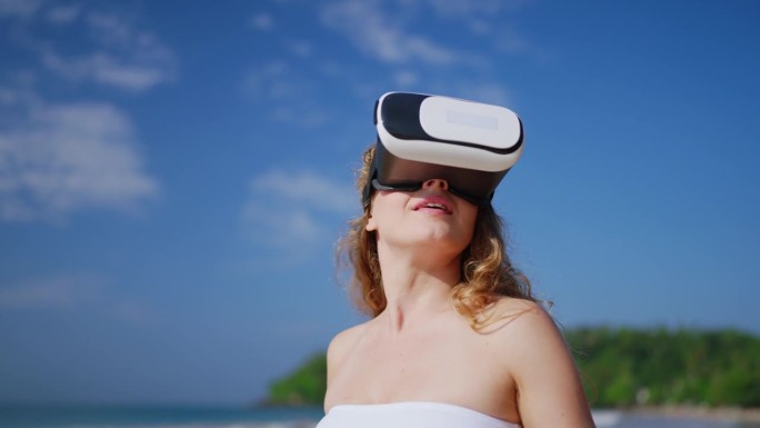 女子沉浸在VR体验中，在阳光明媚的海滩上弯曲手，探索虚拟现实热带模拟。VR头显用户在数字世界中互动，