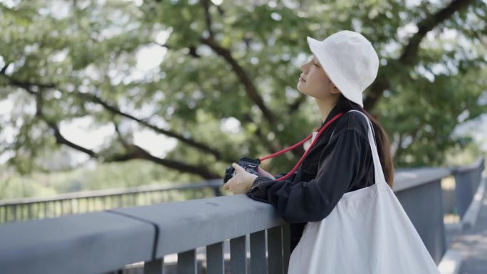 一个穿黑色夹克的亚洲女人站在桥上看着公园在想什么