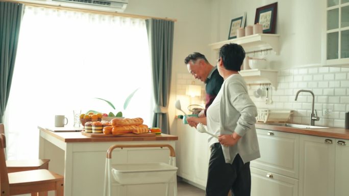 亚洲老年夫妇在家里一起烹饪健康的食物，同时在厨房跳舞的周末早晨，幸福的亚洲老夫妇享受浪漫的老年夫妇跳