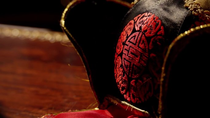 一个华丽的小丑帽的特写与复杂的红色和黑色的图案和金色口音在黑暗的背景。
