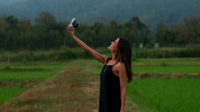 一位年轻女子拿着复古相机在大自然中自拍