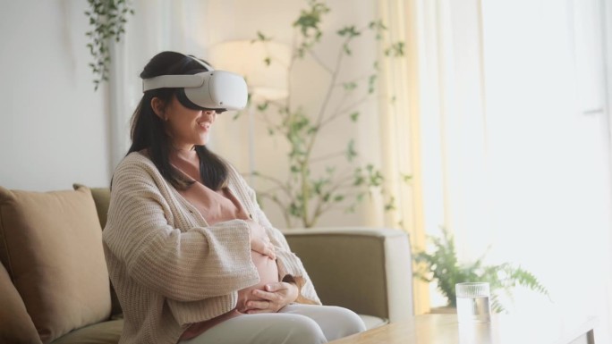微笑的年轻母亲坐在家里的沙发上享受VR现实眼镜。