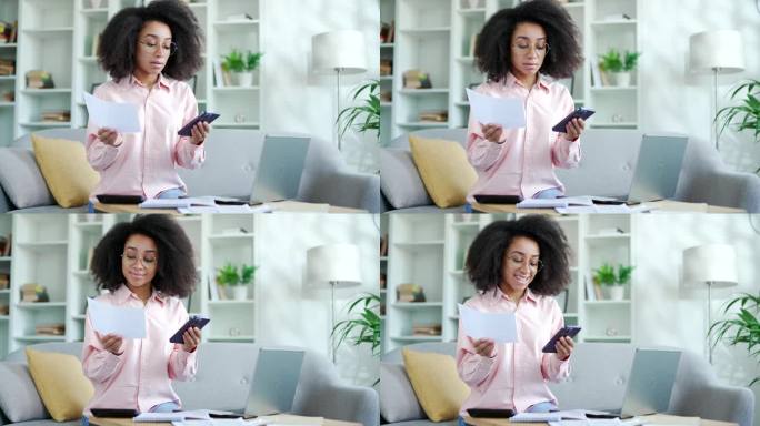 年轻的非裔美国女性坐在家里通过智能手机上的网站或应用程序处理家庭财务