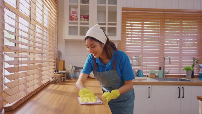 亚洲美女清洁工作和清洁厨房在家里。美丽的管家清洁队穿围裙和清洁肮脏的餐台为客房部的家务和家务。