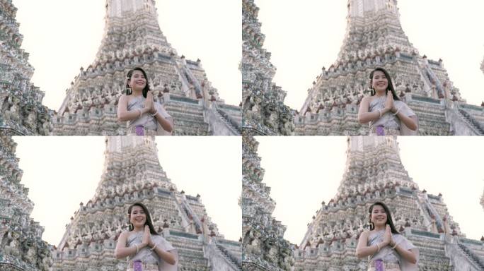 微笑的亚洲妇女在阿仑寺表示敬意，她穿着漂亮的泰国服装