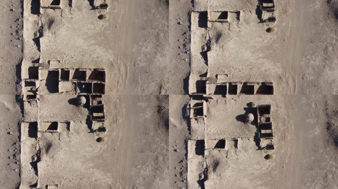 在干燥的沙漠景观中，相机俯视着破败的泥砖土坯建筑，天空湛蓝，没有云