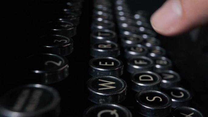 手指正在按下一台20世纪20年代的老式打字机的按键来写文件。唤起侧面细节的特写镜头。