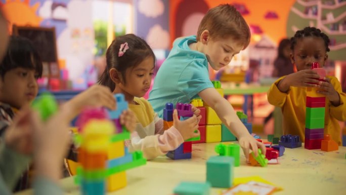 幼儿园小朋友玩五彩积木玩具。美丽的黑人和亚洲女孩和两个快乐的小男孩在现代日托中心一起玩耍