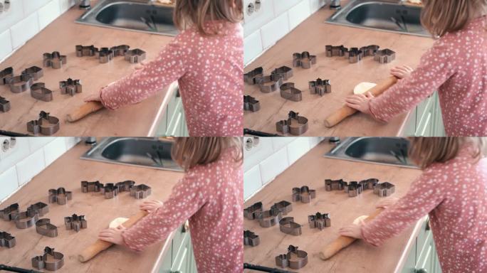 3岁的小女孩站在凳子上，用一根木制擀面杖在厨房的台面上擀出饼干面团。金属烘烤模具。童年烘焙的乐趣，家