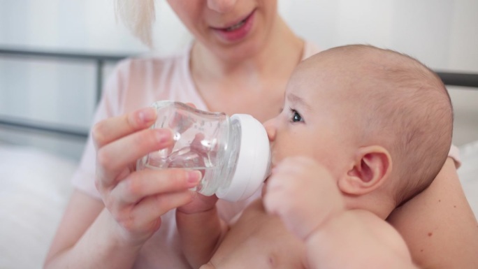 婴儿坐在妈妈的怀里，从奶瓶里喝水