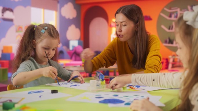 两个可爱的女孩用水彩在纸上创作彩色绘画的肖像。快乐的女教师花时间在幼儿园，教孩子们在美术课上画画