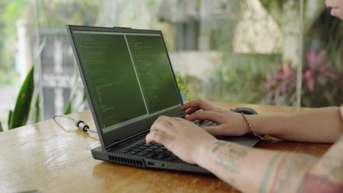 软件开发人员在自然光下在笔记本电脑上输入代码，手指在键盘上飞舞，屏幕上满是编程语法。焦点微妙转移，户