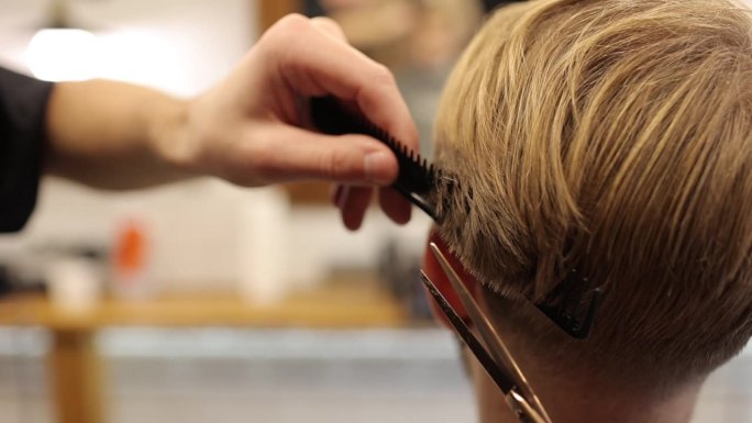 理发师用专业的剪刀和梳子在理发店里剪男人的金发。美发师在沙龙创造现代男性发型。风格与职业理念