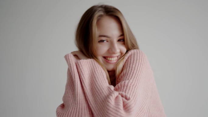 年轻漂亮的女人穿着粉红色的针织毛衣，微笑着看着镜头