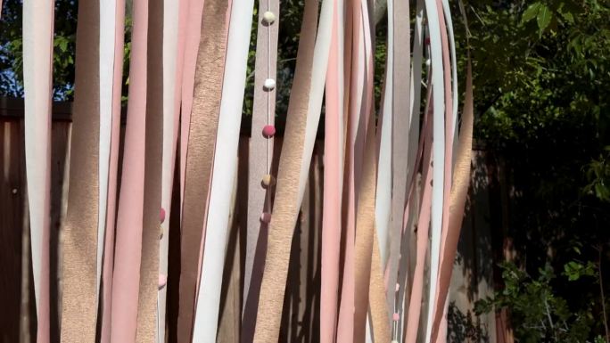 在一个阳光明媚的日子里，DIY粉金色和白色绉纱纸彩带和绒球背景生日派对装饰在微风中流动