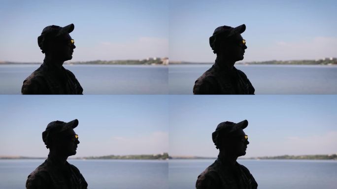 一个身穿军装的乌克兰士兵的剪影，背景是一个湖。这个人戴着战术护目镜。乌克兰武装部队
