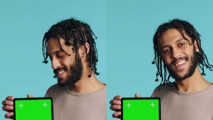 垂直视频男子手持绿色屏幕平板，表现出积极的情绪，工作室背景