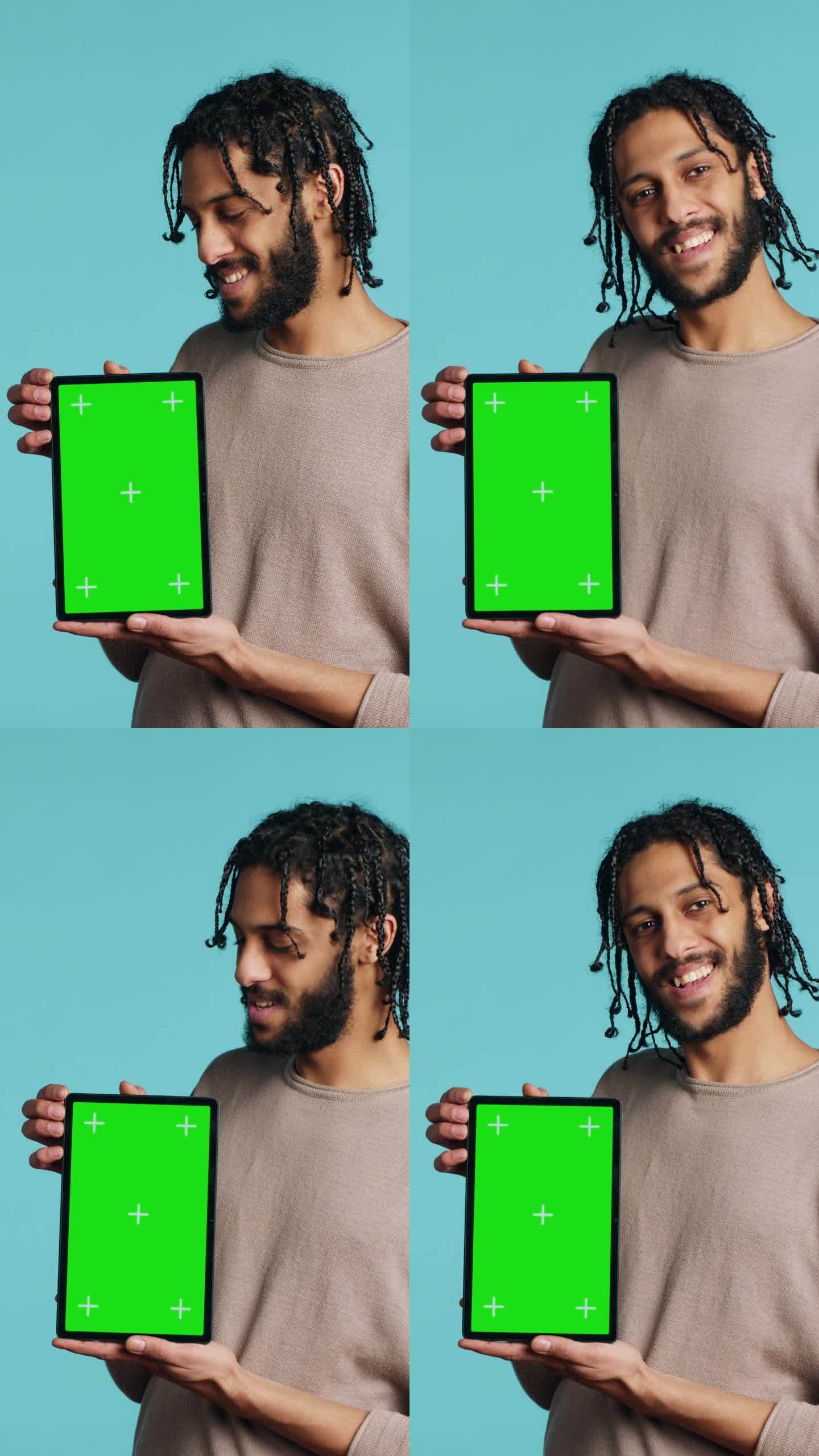 垂直视频男子手持绿色屏幕平板，表现出积极的情绪，工作室背景