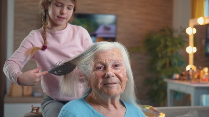 一位90年代的老妇人看着镜头，而她的孙女正在梳理她美丽的白发
