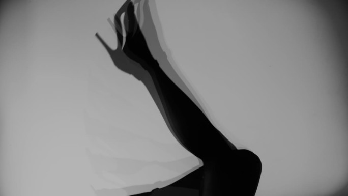 穿着紧身衣和高跟鞋的女人的腿在白色墙壁的背景下移动。黑白照片。