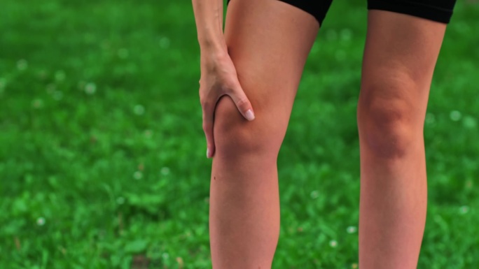 女子在户外草坪上锻炼后膝盖疼痛，用手按摩她的腿。运动理念，养生，运动减肥。