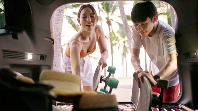 一对快乐的亚洲夫妇从汽车后备箱里拿出一块滑板
