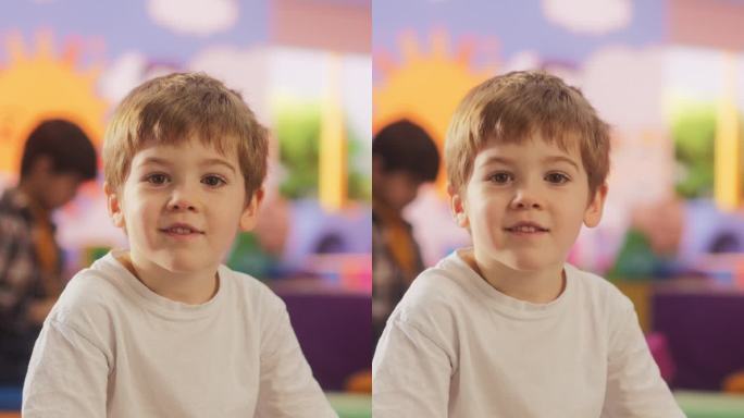 竖屏:一个好奇的白人男孩看着镜头微笑的肖像。在现代幼儿园，天真可爱的小男孩坐在地板上玩积木玩具