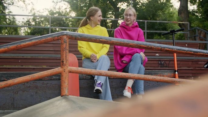 十几岁的女孩朋友坐在滑板车和滑板的论坛上