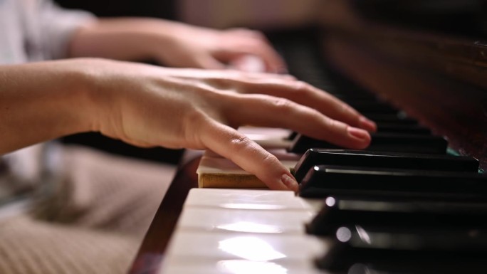 一位年轻女子弹奏复古钢琴的手特写。