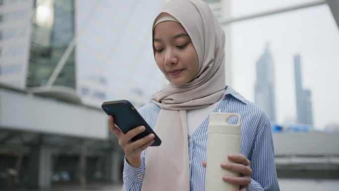 年轻的亚洲穆斯林妇女在户外工作场所使用手机搜索互联网