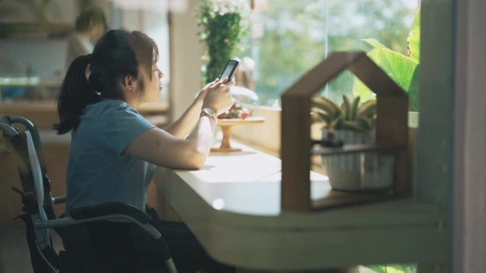 亚洲华裔脑瘫妇女在轮椅上阅读电子书在咖啡馆周末的早晨