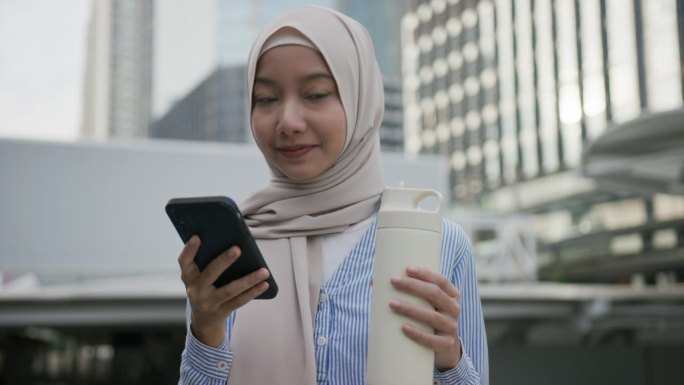 年轻的亚洲穆斯林妇女在户外工作场所使用手机搜索互联网