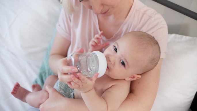 婴儿坐在妈妈的怀里，从奶瓶里喝水