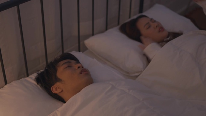 亚洲女人对丈夫晚上睡觉时打鼾感到沮丧。迷人的失眠愤怒的妻子躺在床上，因为噪音无法入睡，在家里的卧室里